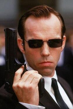 Agent Smith from The Matrix, holding a gun.
