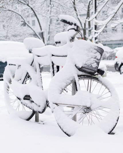 Ein abgestelltes Fahrrad ist fast vollständig von frischem Schnee bedeckt in winterlicher Berliner Stadtlandschaft.