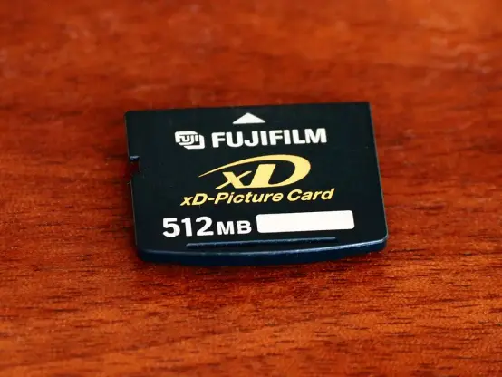Auf einer Holzunterlage liegt eine schwarze xD-PictureCard mit Aufdruck des Herstellers Fujifilm und der Angabe "512MB"