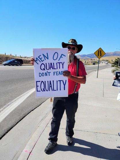 Photo of a man holding a sign that reads: Men of quality don't fear equality.