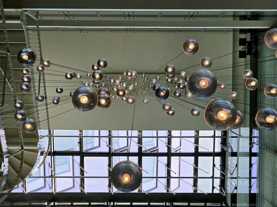 Looking straight up at the ceiling, lots of lamp spheres hanging down in thin wires. Top half of image, the ceiling is concrete, bottom half it is glass.