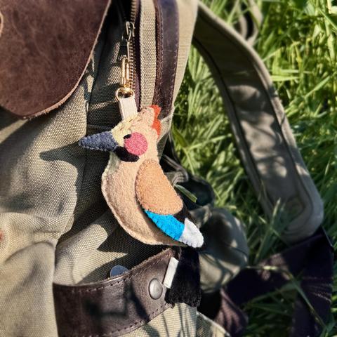 Picture of a handmade felt bag charm in the shape of a Eurasian jay with a cream-coloured body, a grey beak, a reddish crest; and a bright blue stripe on its wing. The charm is attached to a green backpack that is set in the grass. Picture of a handmade felt bag charm in the shape of a Eurasian jay with a cream-coloured body, a grey beak, a reddish crest; and a bright blue stripe on its wing. The charm is attached to a green backpack that is set in the grass.
