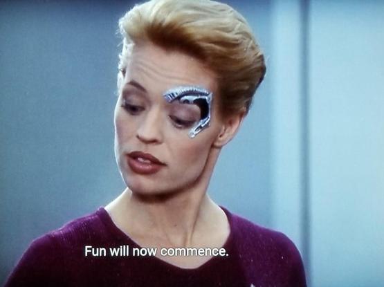 Star Trek Voyager scene. Seven of Nine (tertiary adjunct of unimatrix 01) is pictured. She has a dolphin shaped metal robotic implant around her left eye because she is a borgs. Closed caption reads, "Fun will now commence."