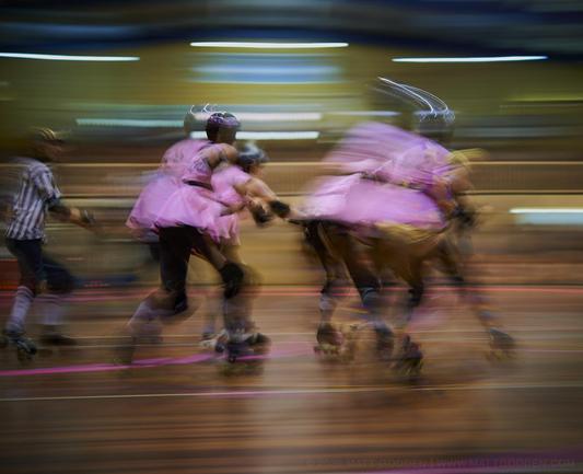A long exposure image of roller derby competitors from the Beauty School Knockouts (pink), and Team Unicorn (Purple & Gold). 2013/11/09