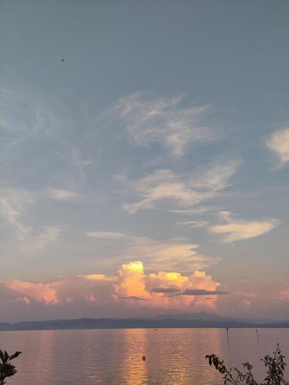 Zu sehen ist der Blick über den See in Abendstimmung. Am Horizont sind Dichte Wolkenformationen, die gelb-gold leuchten.