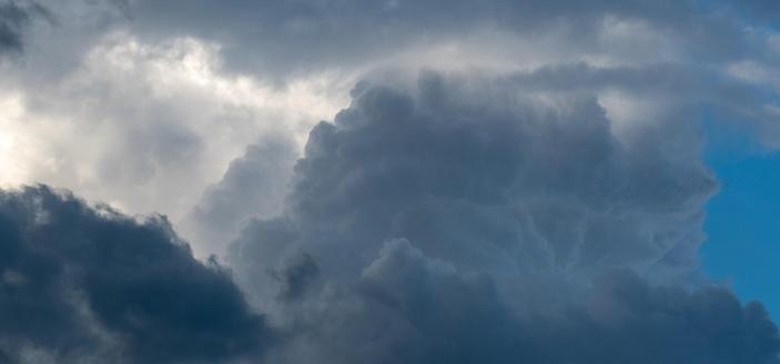 Dense, billowing, overlapping clouds from dark grey to shining white, blue sky at the far right.