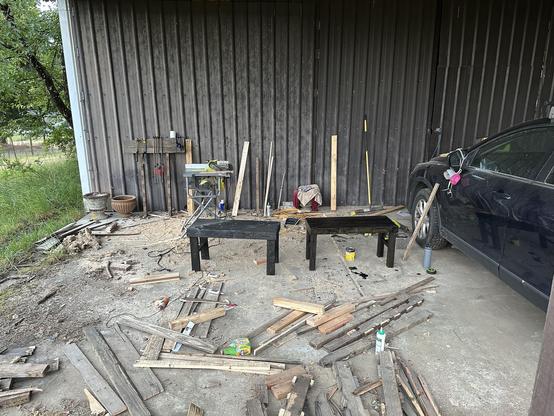 The concrete floor in front of the barn again, but all the palettes have been broken down (with the wood largely in piles on the floor). Two short black benches are in the middle of the frame.