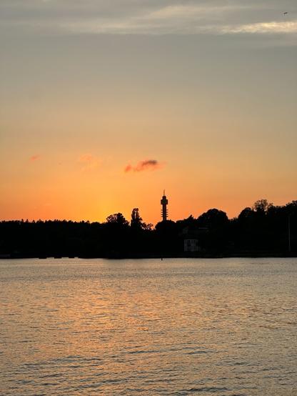 a small cloud, backlit by the setting sun, floating over the silhouette of a geometric tower on the far shore of a body of water. The sky is golden, and the light reflects in the water