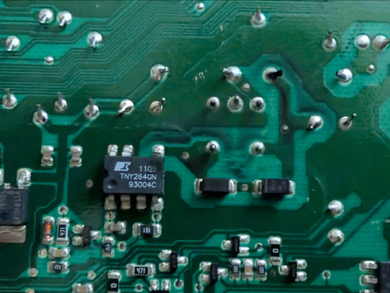 Ausschnitt eines PCBs einer Waschmanschine. In der Mitte ein Bauteil mit einer verkohlten Ecke und schwarzen Spuren drumherrum.