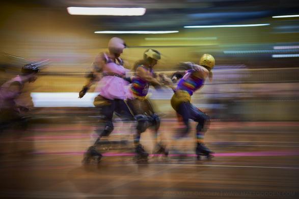 A long exposure image of roller derby competitors from the Beauty School Knockouts (pink), and Team Unicorn (Purple & Gold). 2013/11/09