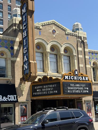 Marquee of an old movie theater. The vertical part says “Michigan “ in white letters on blue background. The awning says “Happy birthday, Mel Brooks! Producers 1:30 pm”