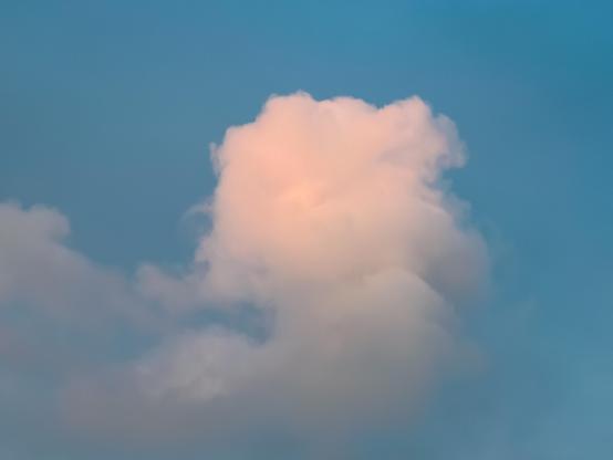 A fluffy cloud almost pink at sunset in a blue sky