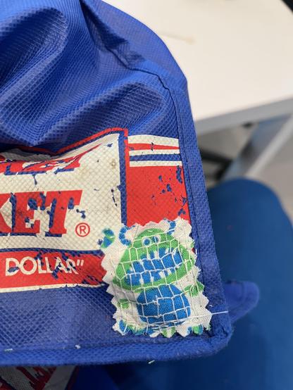 The patch had been fully sewn in place with a little mesh network of blanket stitches. The patch fabric has a little green and blue monster with striped horns and a round belly and big gappy teeth.