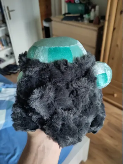 Front view of a Dark Souls' Crystal Lizard plushie.
In the game, it's a small creature resembling a chunky lizard, but it's fully made of rock and crystals.
Its body is a dark grey with bright cyan-colored gems.
Its plushie body is made of soft fur made to resemble rough rough and the gems are smooth, shiny fabric. They have different segments so they look faceted.
It has tiny limbs.