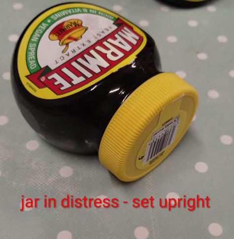 A Marmite jar on its label, most likely knocked over. Text reads "jar in distress - set upright".