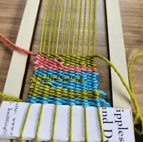 A really small loom with some weaving in turquoise, green and pink/orange