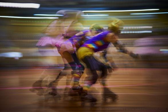A long exposure image of roller derby competitors from the Beauty School Knockouts (pink), and Team Unicorn (Purple & Gold). 2013/11/09
