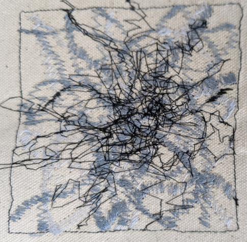 A tangle of stitched lines using free zigzag in cream, grey and black thread on an off-white background fabric. A concentrated area in roughly the centre like knotted threads.