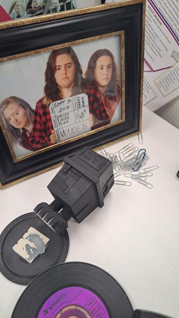 A photo of a corner of my desk, where my 3d printed Gonk Droid from Star Wars is lying on its side. Since I use it to store paperclips, they are scattered across the desk.