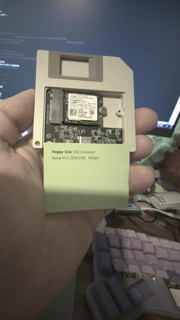 gray floppy disk shaped object with an adapter pcb inside and a 2230 m.2 SSD mounted to it, light lime colored cover