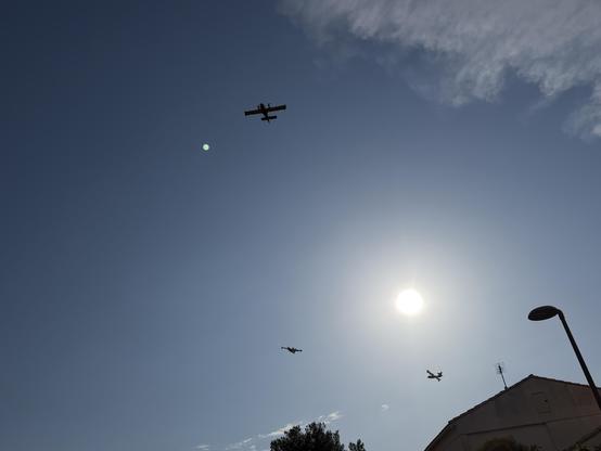 trois canadairs volent dans un ciel clair au soleil brillant