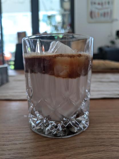 Tumbler glass holding a perfectly layered iced latte, i.e. with a layer of coffee swimming on milk