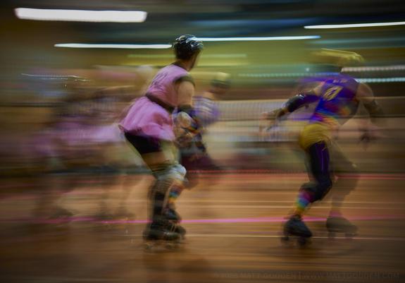 A long exposure image of roller derby competitors from the Beauty School Knockouts (pink), and Team Unicorn (Purple & Gold). 2013/11/09