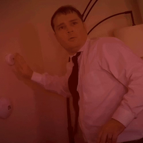 A man repeatedly pushing a button on the wall while looking intently and a bit confused.