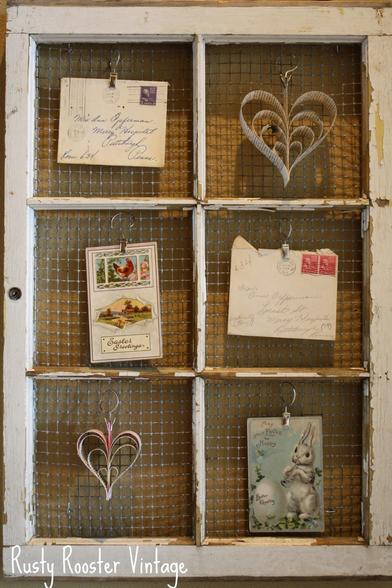 Glassless old window say, tiled, metal mesh behind, adorned with antique postcards and heart-shaped paper decorations, decorative overall
