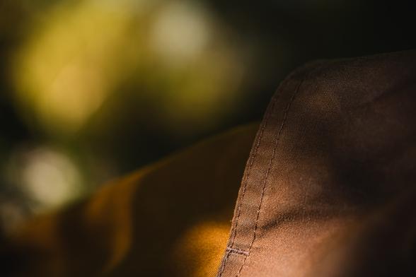 A close up photograph of part of a pair of trousers. There are two different colour materials, bot from sturdy, tightly woven cloth. Over the knee part, a brown colour and lower an almost golden amber. The textile is partly sunlit, partly in shadow, partly in focus and partly out of focus.

The trouser leg pictured fills a roug diagonal in the lower part of the frame and the background has a few patches of bright, blurry bokeh discs in white/yellow/greenish colours, surrounded by dark areas.