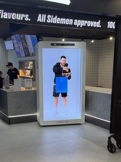 inside a fast food restaurant with vaguely futuristic decor, there’s a holographic display showing a lifesize 3D projection of a man holding a cardboard tray of fries, with a blue interface floating in front of him