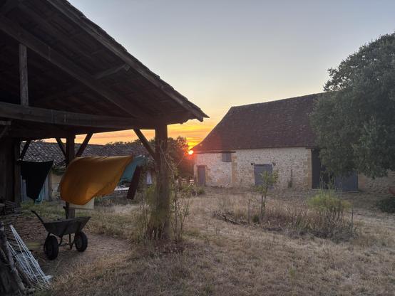 Coucher de soleil orangé entre un préau et une ferme.