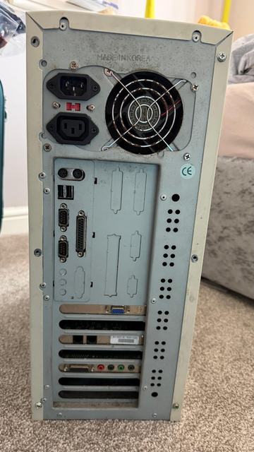 A photo of the rear of a typical early 2000s PC tower case. At the top is the power supply exhaust fan grille and you can see black grime encrusted around the metal.
