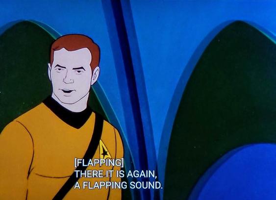 Star Trek The Animated Series scene. Cartoon Kirk is standing in his gold uniform, and has a man satchel over a shoulder. Behind him is a green and blue archway/wall design. Closed caption reads, "[FLAPPING] There it is again, a flapping sound."