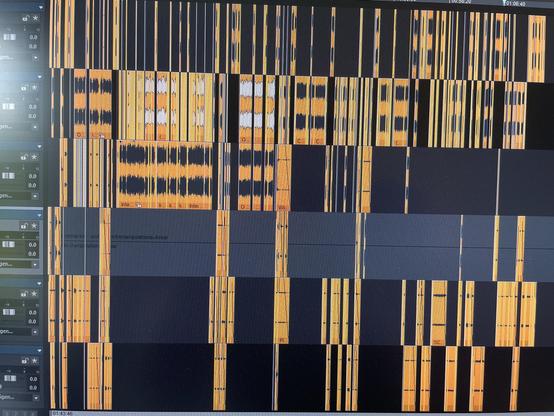 Das Bild zeigt eine Audiobearbeitungsoberfläche mit mehreren Spuren, die als Wellenformen dargestellt werden. Die Wellenformen sind überwiegend in Orange und Gelb vor einem dunklen Hintergrund gehalten, mit unterschiedlichen Längen und Mustern, die auf verschiedene Audiosegmente hinweisen. Auf der linken Seite sind Beschriftungen und Zeitstempel sichtbar.