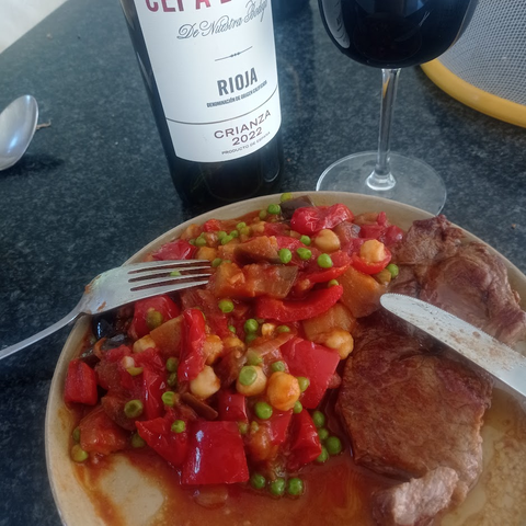 un guiso de mimientos y tomates, garbanzos, guisantes. Tamnien hay pimienton picante y laurel.  Tambien se vé un vaso de vino con su botella, rioja crianza.
