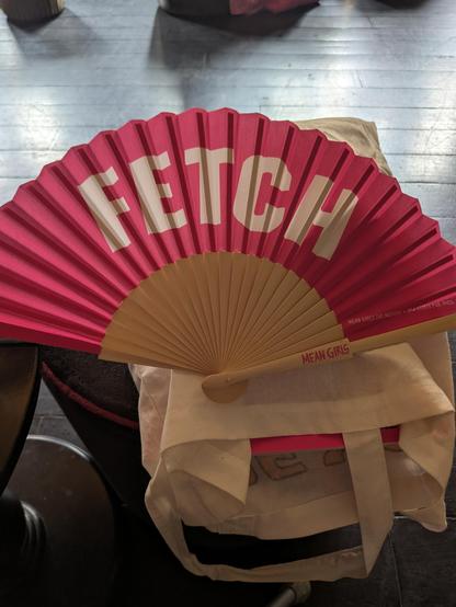 A paper and light wood fan. The paper is pink and says "Fetch" on it.