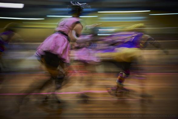 A long exposure image of roller derby competitors from the Beauty School Knockouts (pink), and Team Unicorn (Purple & Gold). 2013/11/09
