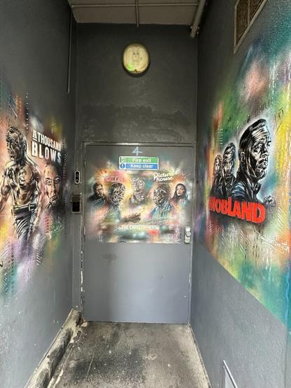 a narrow space with three grey walls, as if of temporary hoarding, and a door at the end. All three walls have colourful stencil art, with black shapes and white highlights against backgrounds of multi-coloured spray paint. The pieces resemble film posters in format and bear the titles “A Thousand Blows”, “The Christophers” and “MobLand”, with the likenesses of actors in their roles
