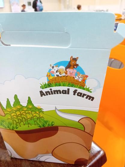 Child's lunch box, featuring colourful cartoon agricultural animals looking over a fence, and the legend "Animal Farm". George Orwell is spinning in his grave.