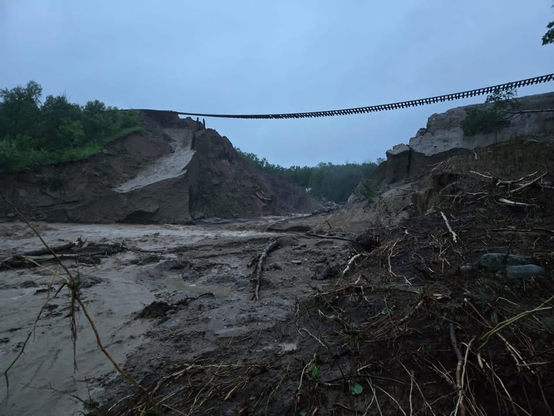 Train tracks suspended dozens of feet in the air over a washed out embankment at a water course, from flooding.