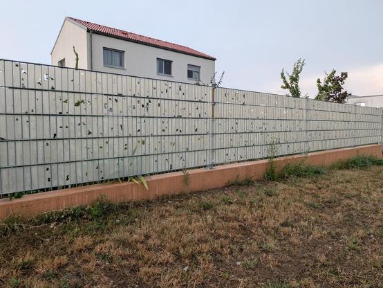 A double-bar fence with light grey privacy strips. The privacy strips are full of holes, just like Swiss cheese.