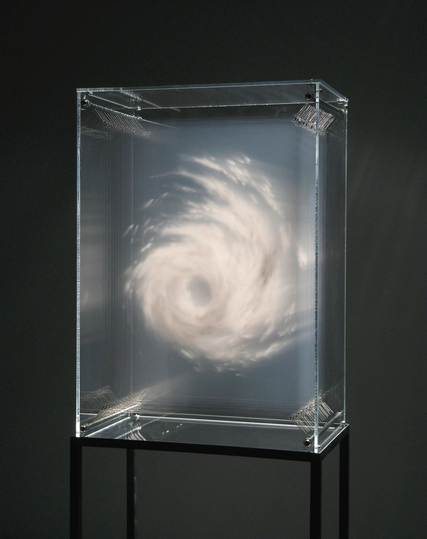 A conceptual art piece showing a transparent, rectangular acrylic case mounted on a slender black metal stand against a gray backdrop. Inside the clear box, a white, cloud-like swirl resembles a miniature hurricane or vortex suspended in mid-air.