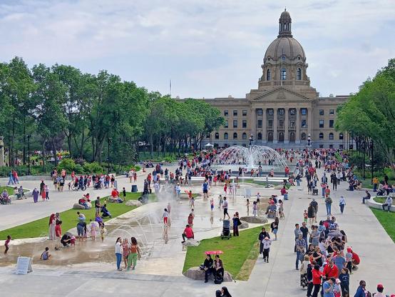 The Alberta Legislative grounds in Edmonton, AB from a high perspective, showing a large crowd of people around the public fountains and pools.