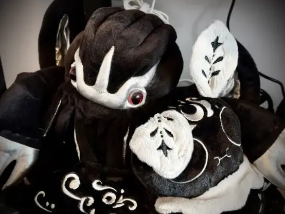 A black and silver Cthulhu plush hugging a black and silver moth person plush.