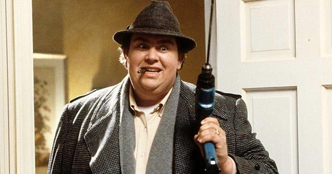 Screen shot of scene from Uncle Buck.  John Candy is in a goat and a hat standing in a doorway.  He has an excited look in his eyes, a cigar in his mouth and is holding up a power drill.