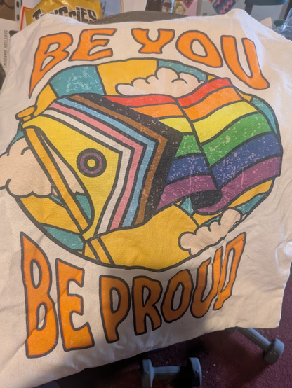 A white tote bag with the Pride Inclusive flag on it along with the words "Be you, Be proud".