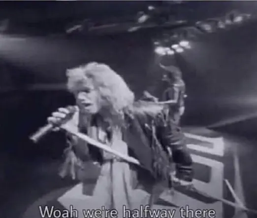 A screenshot from Bon Jovi's music video for the song "Livin' on a preayer", where he is standing on a stage and singing: "Woah we're halfway there."