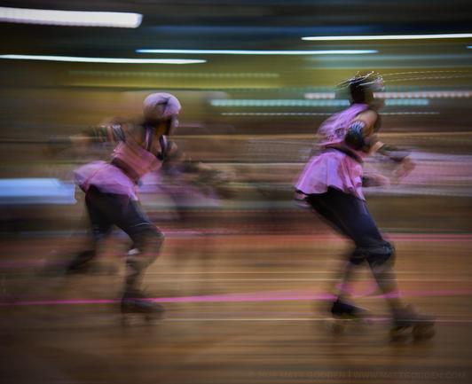 A long exposure image of roller derby competitors from the Beauty School Knockouts (pink), and Team Unicorn (Purple & Gold). 2013/11/09