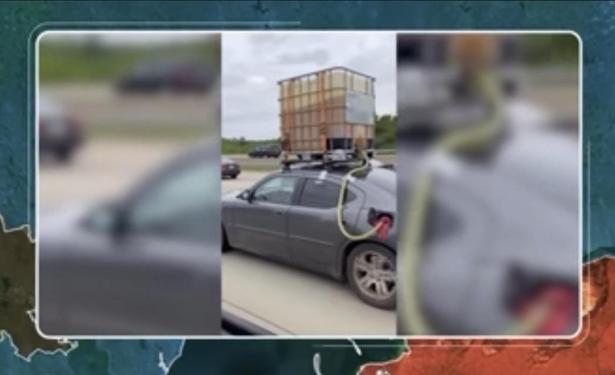 A car on a highway with a large, wood-plastic-metal container mounted on its roof, connected to the car's fuel system with tubes. Other vehicles can be seen in the background.